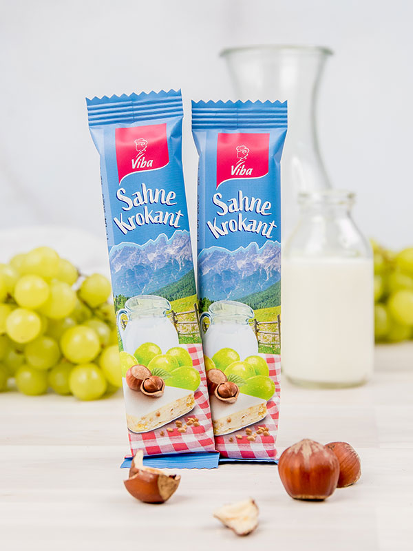 Viba Genussriegel Sahne-Krokant steht vor Trauben und einer Milchkanne