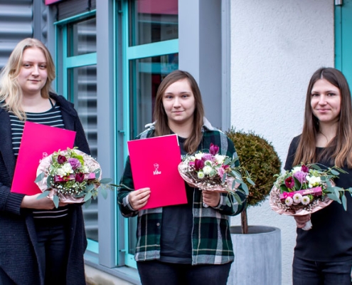 Drei Absolventinnen bei Übergabe der Blumensträuße