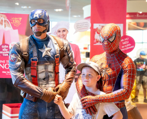 Superhelden-in-der-Nougat-Welt Captain America und Spider-Man posieren mit einem Jungen vor dem Shop der Nougat-Welt