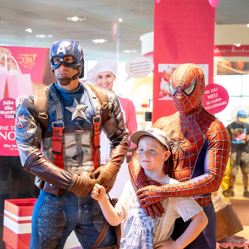 Superhelden-in-der-Nougat-Welt Captain America und Spider-Man posieren mit einem Jungen vor dem Shop der Nougat-Welt